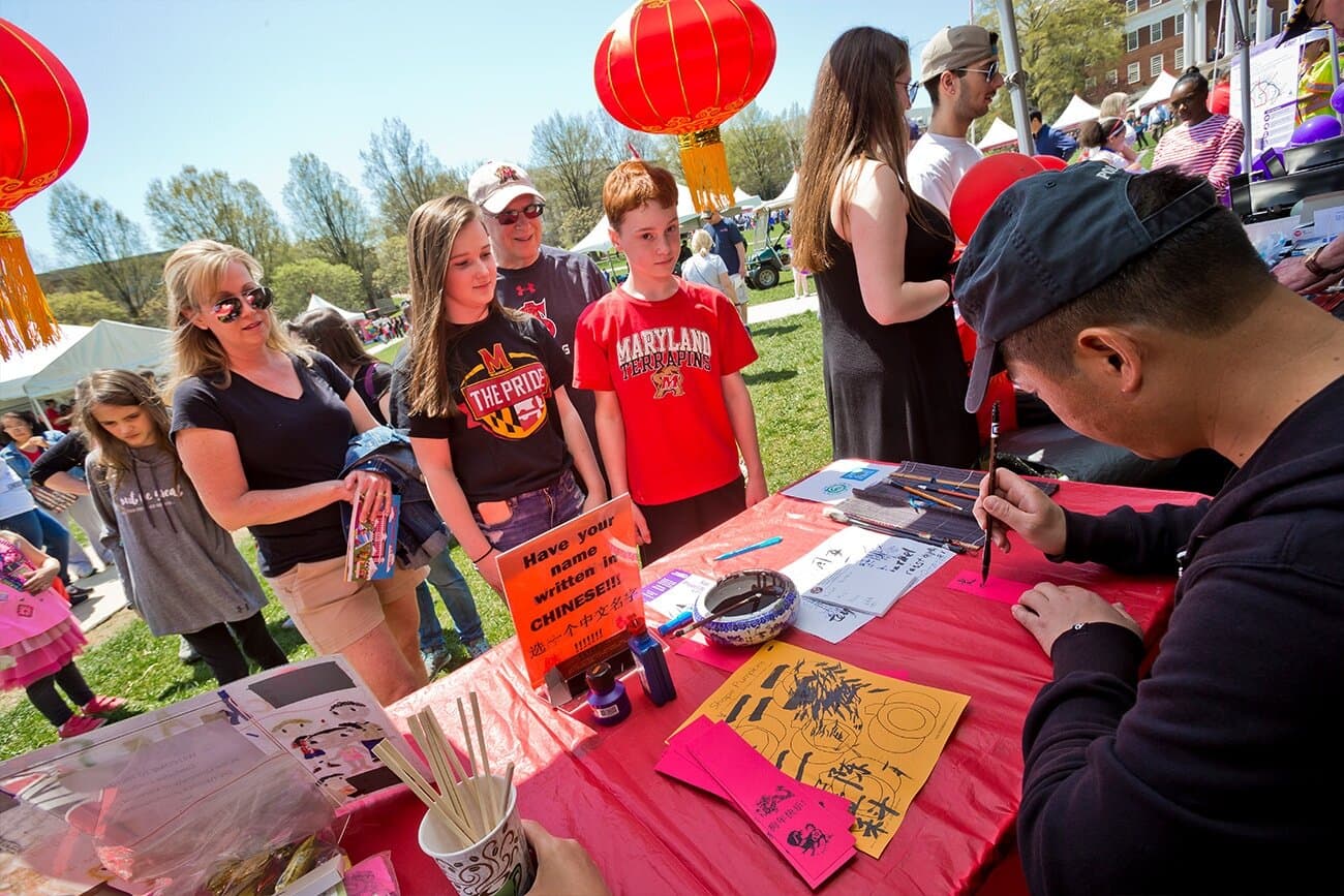 Maryland Day attendees watch with focused curiosity as they have their name translated into traditional Chinese by an event volunteer