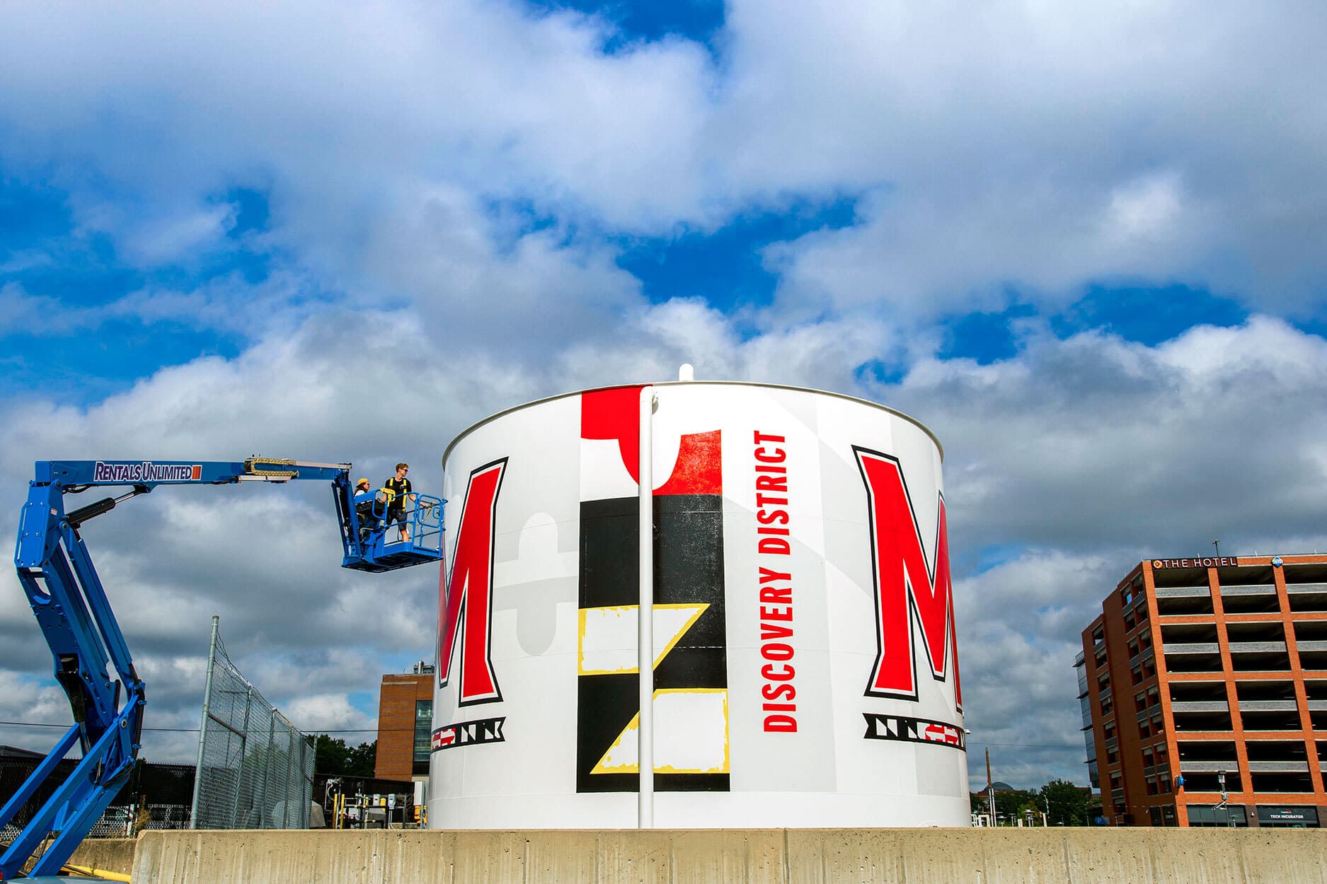A water tower in College Park's discovery district encompassed by graphics of the Maryland M logo and Maryland flag graphics