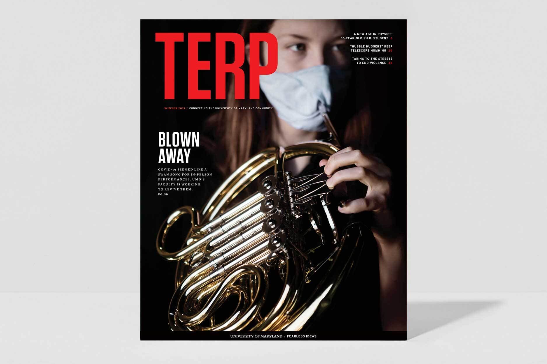 Terp Magazine Winter 2021 edition, cover page. A student plays a German horn through a small opening in the face-mask they're wearing.